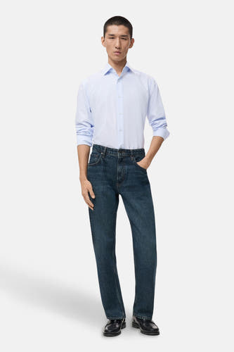 Chemise rayée bleue de MANGO avec des manches longues, portée avec des jeans foncés et des chaussures noires.