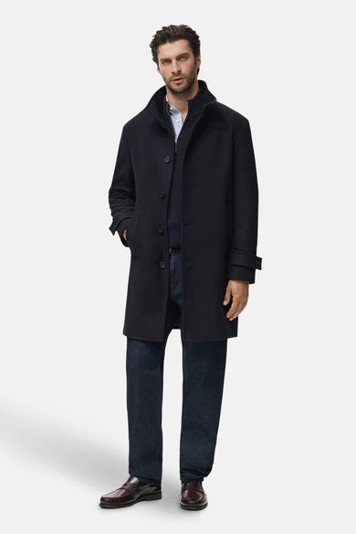 Blauwe lange jas van MANGO, gedragen met een overhemd, trui en donkere jeans, met bruine loafers.