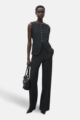 Veste grise chinée de MANGO, portée avec un pantalon large et sombre et des chaussures pointues, avec une poche main noire.