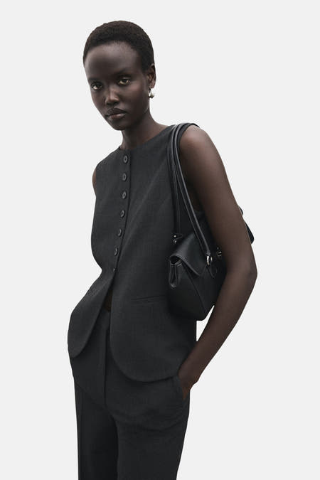 Blazer gris de MANGO porté par un modèle avec un sac noir et une pantalon coordonné.