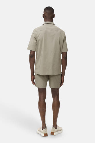 T-shirt kaki avec manches courtes de MANGO, vu de derrière, avec des shorts coordonnés et des baskets crème.