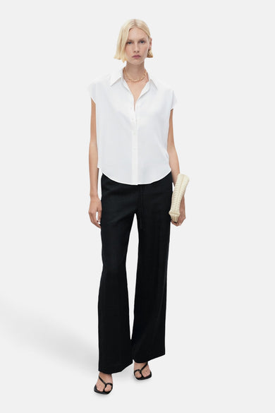 Blouse blanche sans manches de MANGO, avec une chaîne d'or et un sac à main beige.