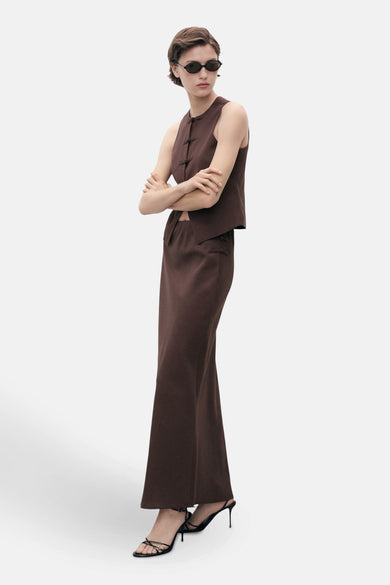 Long manteau brun de MANGO, associé à une chemise brune et des bottes noires.