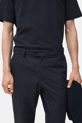 Pantalon bleu de MANGO, avec une texture lisse et une fermeture à boutons, porté avec un chemisier bleu marine.