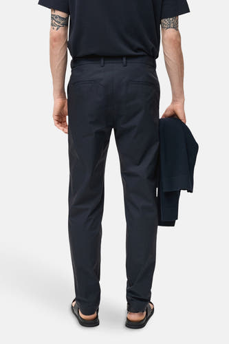 Pantalon bleu de MANGO, vu de de dos, avec un blouson froissé dans la main et des sandales.