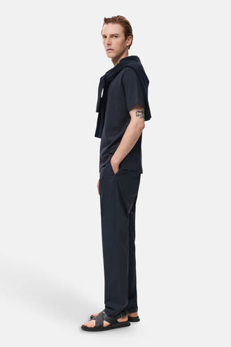 Pantalon bleu de MANGO porté avec un T-shirt bleu marine et des sandales, en vue latérale.