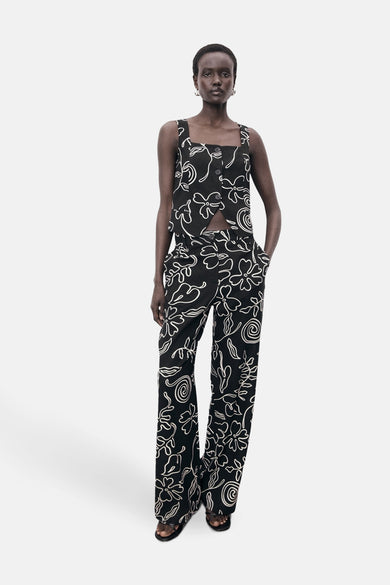 Blouse noire sans manches de MANGO avec un motif de fleurs blanches, associée à une jupe coordonnée.