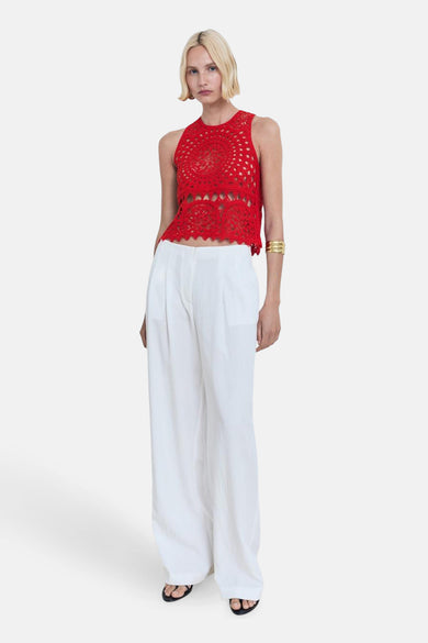 Blouse sans manches rouge de MANGO, avec un motif tricoté, portée avec un pantalon blanc et des sandales.
