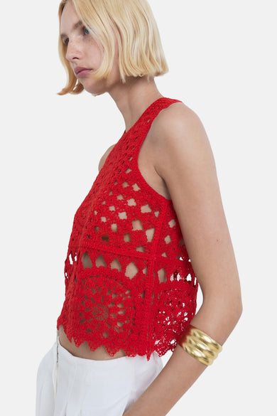 Blouse sans manches rouge de MANGO, avec un motif en mailles ouvertes et portée avec un bracelet doré.