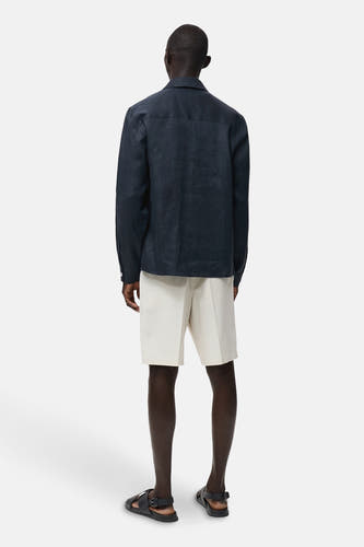 Chemise bleue marine à manches longues de MANGO, vue de derrière, associée à un short blanc et des sandales noires.
