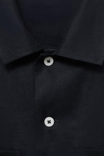 Chemise bleue marine à manches longues de MANGO, avec un col ouvert et deux boutons blancs.