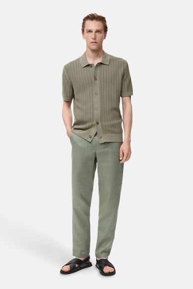 Chemise kaki à manches courtes de MANGO, avec col boutonné et portée avec un pantalon en lin et des sandales.