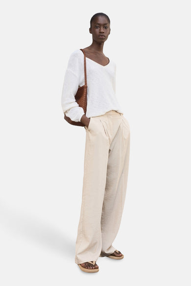 Pantalon beige de MANGO, avec des jambes larges et une taille pliée, porté avec un pull blanc et un sac marron.