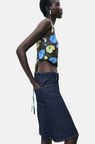 Blouse multicolore sans manches de MANGO, à imprimé floral, boutonnée sur le côté, portée avec une jupe bleu marine.