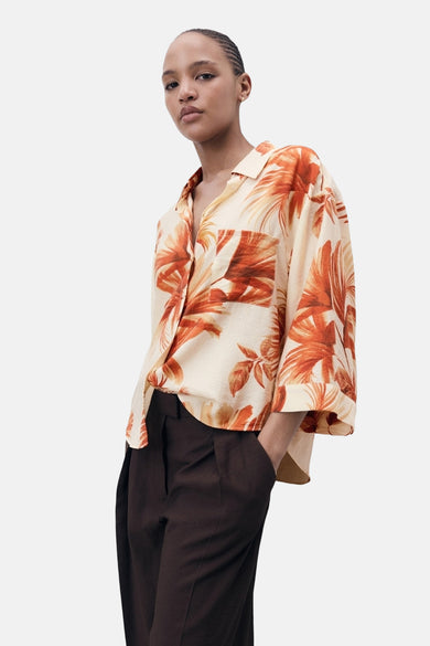 Chemise multicolore à manches courtes de MANGO, avec imprimé feuille et portée avec un pantalon foncé.