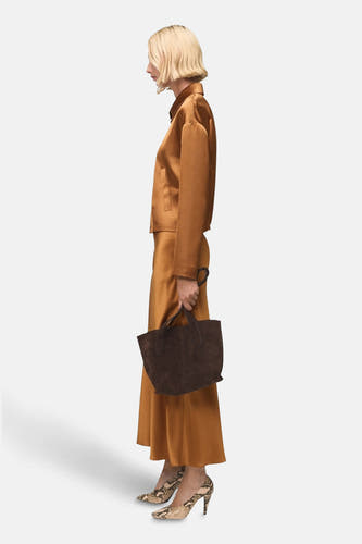 Long manteau brun de MANGO, avec un aspect soyeux et porté avec une poche main brun et des escarpins en cuir de serpent.