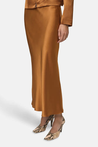 Long manteau brun de MANGO, avec une texture lisse et un subtil éclat, associé à des escarpins imprimés serpent.