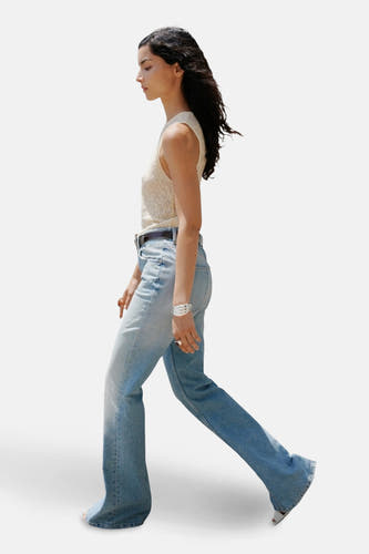 Flared jeans van lichtblauw denim van MANGO, met een bruine riem, en een witte top.
