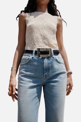 Jean flare bleu clair de MANGO, avec une ceinture noire et une boucle argentée, porté avec un haut en dentelle.