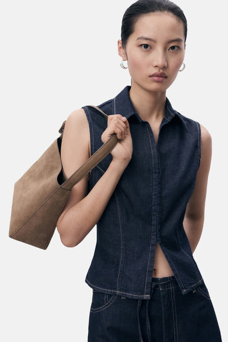 Chemise bleue marine sans manches de MANGO, portée avec un sac en cuir marron sur l'épaule.