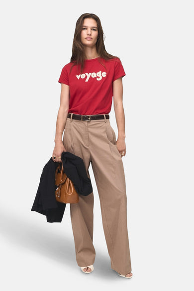 T-shirt rouge à manches courtes de MANGO avec une impression blanche "voyage", associé à un pantalon marron et des accessoires.
