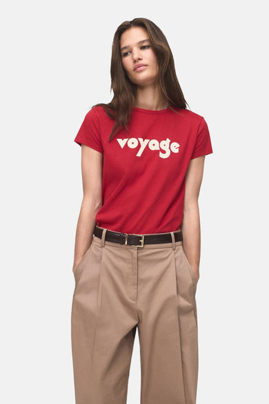 T-shirt rouge à manches courtes de MANGO, avec le texte "voyage" en lettres blanches, porté avec un pantalon marron.