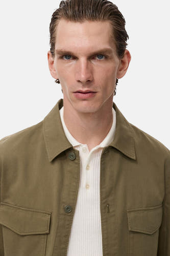 Chemise verte (manches longues) de MANGO, portée sur un polos rayé blanc avec col.