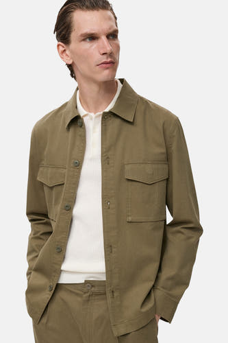 Chemise verte à manches longues de MANGO, avec des poches sur la poitrine et portée sur un polo blanc.