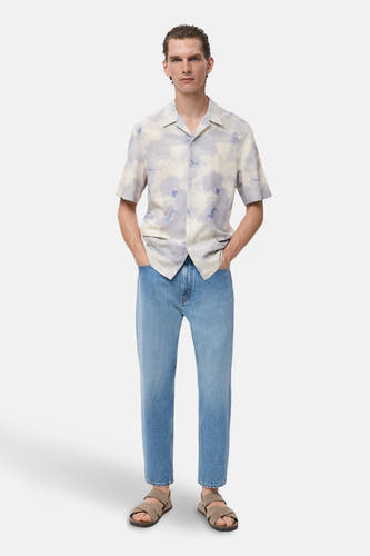 Chemise multicolore à manches courtes de MANGO, avec un motif nuageux abstrait, associée à des jeans bleu clair et des sandales.