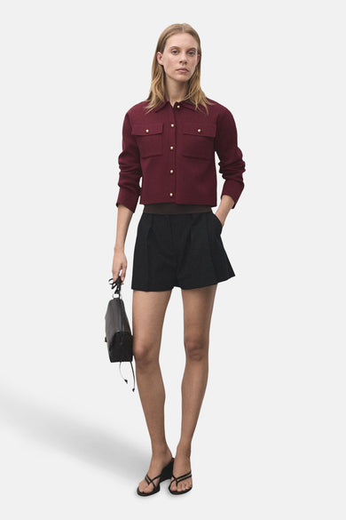 Bordeaux cardigan van MANGO, met lange mouwen en goudkleurige knopen, gecombineerd met zwarte shorts en sandalen.

