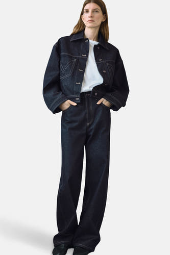 Veste en jeans bleu marine de MANGO, avec des surpiqures blanches et portée sur un t-shirt blanc et des jeans noirs.