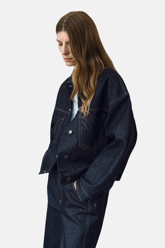 Manteau de denim bleu marine MANGO, avec des manches longues et des boutons contrastés, porté avec une chemise bleue claire.