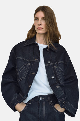 Veste en jeans bleu marine de MANGO avec des boutons contrastants et une fermeture à glissière, portée sur un T-shirt blanc et des jeans.