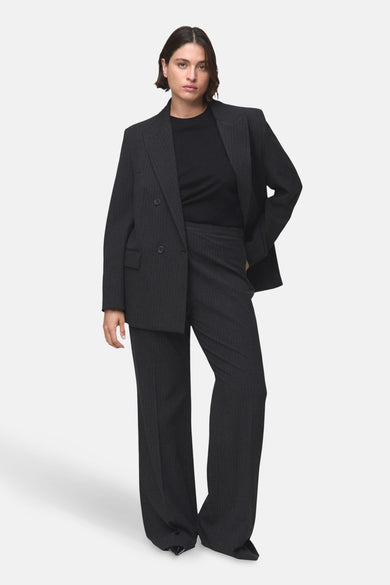 Pantalon gris de costume MANGO, avec une rayure blanche et des jambes larges, associé à un t-shirt noir et un blazer.