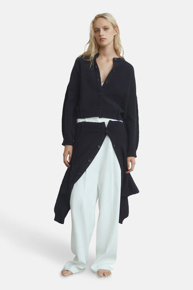 Gilet bleu de MANGO porté sur une chemise blanche et un pantalon blanc large.