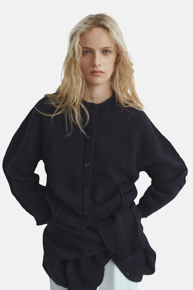Gilet bleu de MANGO, avec fermeture à boutons et longues manches, porté sur une jupe coordonnée.