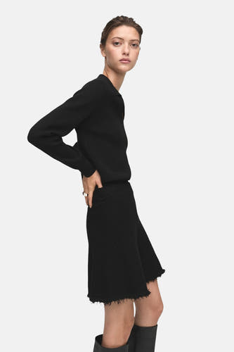 Jupe courte noire de MANGO avec un volant, associée à une veste noire et des bottes jusqu'aux genoux.