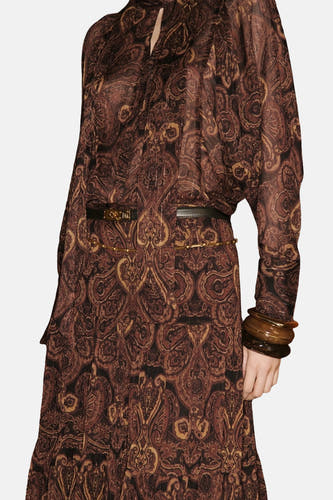 Blouse brune à longues manches de MANGO, avec un motif paisley, une ceinture noire et des bracelets bruns.