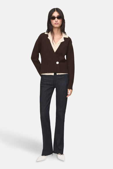 Gilet marron de MANGO, associé à une blouse crème, un pantalon en jean foncé et des chaussures blanches.