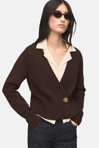 Gilet marron de MANGO avec une seule bouton doré, porté sur une blouse claire et des jeans foncés.