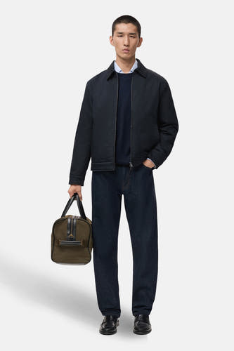 Courte veste bleue de MANGO, avec une fermeture éclair et portée avec un pull bleu, des jeans et des loafers.