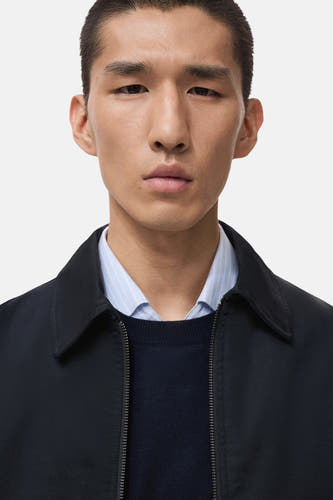 Manteau court bleu de MANGO porté sur un pull bleu et une chemise à carreaux.