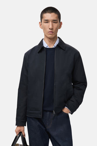 Manteau bleu court de MANGO porté sur une chemise bleue foncée et un blazer bleu clair, avec des jeans noirs.