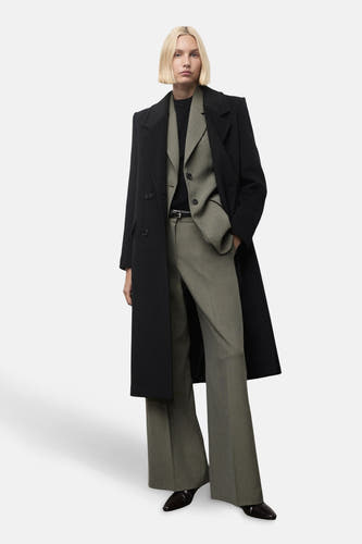 Groene broek van MANGO, gecombineerd met een blazer en zwarte jas, staand op een witte achtergrond.