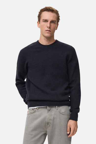 Donkerblauwe trui met ronde hals van MANGO, gecombineerd met een wit T-shirt en grijze jeans.
