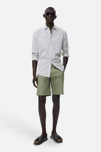 Short vert de MANGO, porté avec un chemisier rayé et des sandales en cuir.