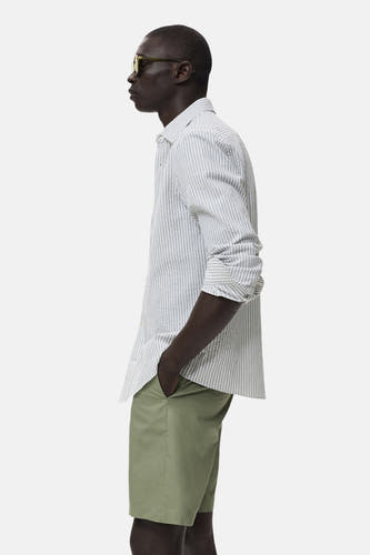Short vert de MANGO, avec une couleur unie et une coupe classique, porté avec un chemisier rayé.