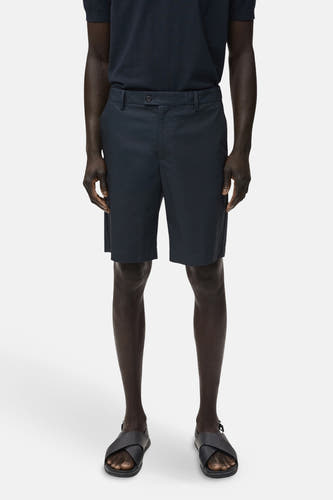 Short bleu de MANGO porté avec un poloshirt bleu marine et des sandales noires sur un fond blanc.