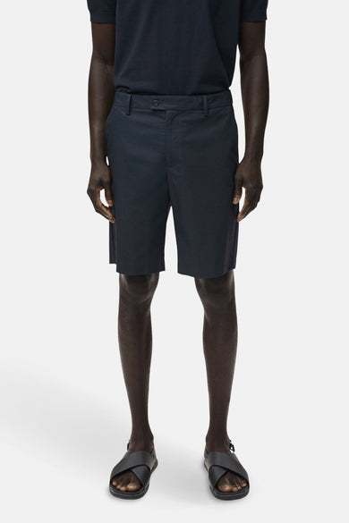 Short bleu de MANGO porté avec un poloshirt bleu marine et des sandales noires sur un fond blanc.