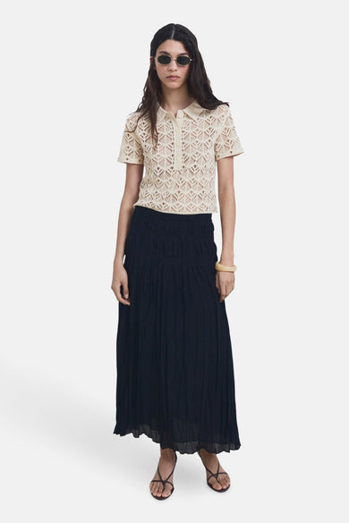 Pull beige à col rond de MANGO, avec un motif ajouré et des manches courtes, associé à une longue jupe sombre et des sandales.